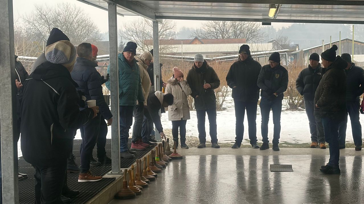 Eine Gruppe von Menschen in Winterkleidung steht in einer Reihe, wahrscheinlich um an einem Spiel teilzunehmen oder an einer Veranstaltung teilzunehmen. Einige von ihnen halten Tassen. Sie befinden sich in einem Außenbereich mit Schnee auf dem Boden.