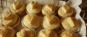 Ein Tablett mit herzförmigen Cupcakes mit Sahneglasur, auf einem weißen Tuch angeordnet.