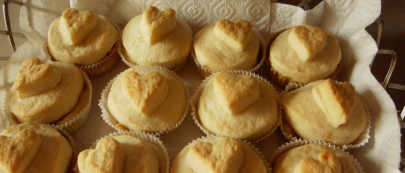 Ein Tablett mit herzförmigen Cupcakes mit Sahneglasur, auf einem weißen Tuch angeordnet.