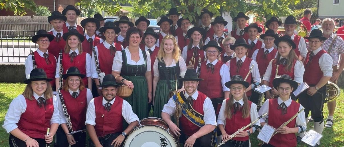 Eine Gruppe von Musikern in traditioneller Kleidung, einschließlich roter Westen und Hüten, posiert für ein Foto unter einem Baum. Einige halten Musikinstrumente.