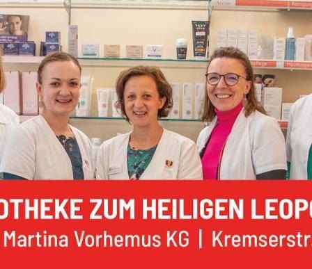 Fünf Frauen in weißen Laborkitteln stehen vor einer Apotheke mit Regalen voller Produkte im Hintergrund. Der Text lautet Stadtapotheke zum Heiligen Leopold.