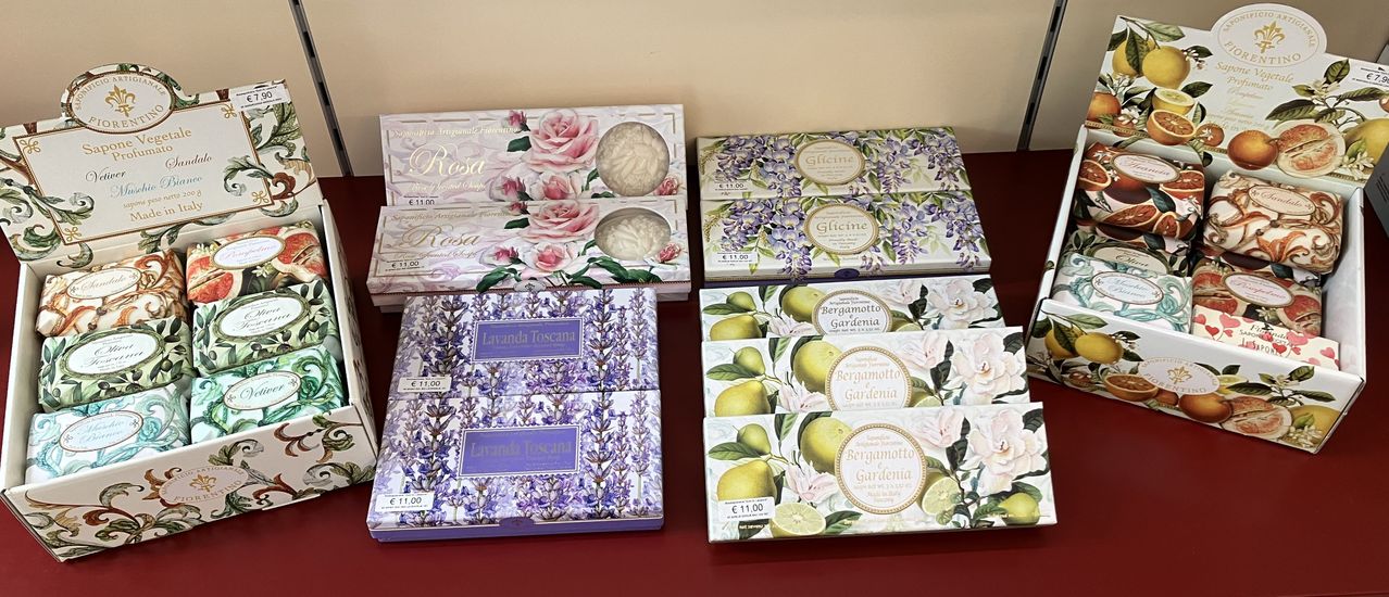 Eine Präsentation von vier Schachteln mit duftenden Seifen mit Blumendesigns. Die Schachtel oben links hat ein Rosendesign und ist mit Rosa beschriftet. Die Schachtel oben rechts hat ein lila Blumendesign und ist mit Glicine beschriftet. Die Schachtel unten links hat ein Lavendeldesign und ist mit Lavanda Toscana beschriftet. Die Schachtel unten rechts hat ein Zitronendesign und ist mit Bergamotto Gardenia beschriftet.