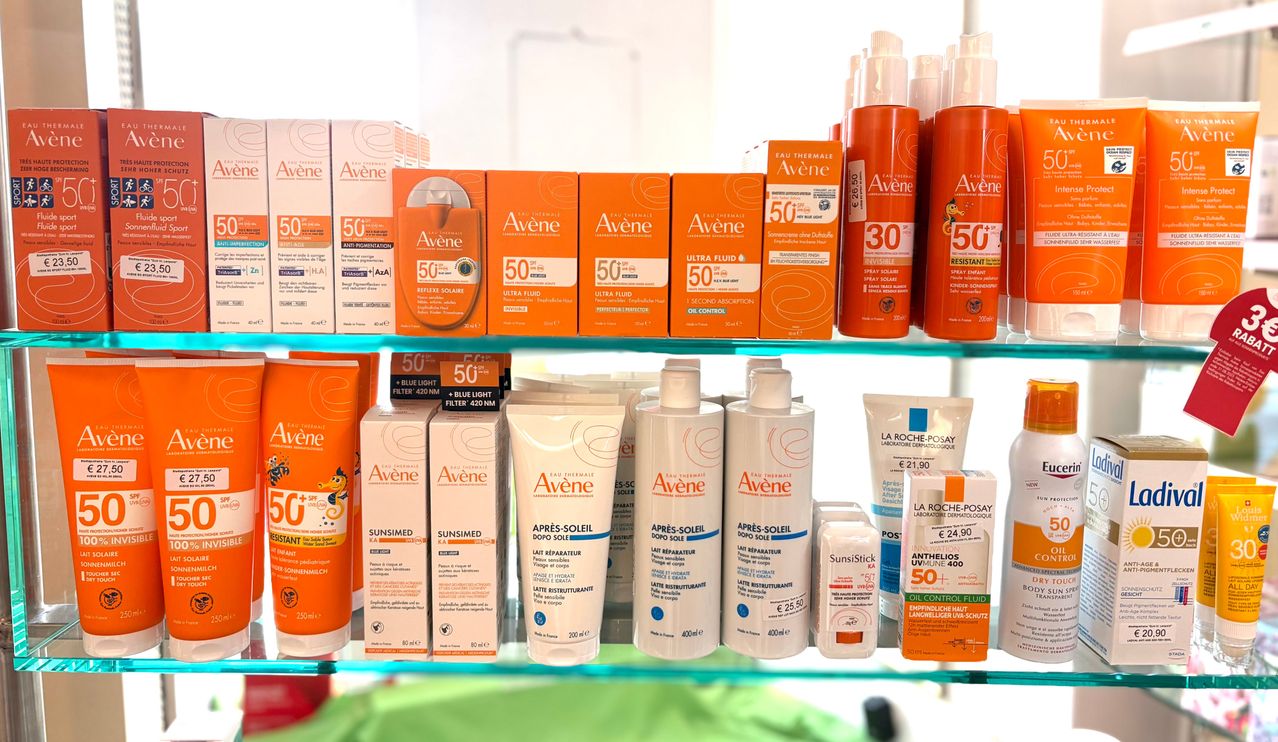 Ein Regal zeigt verschiedene orangefarbene und weiße Sonnenschutzprodukte, einschließlich Avene Sonnencreme mit LSF 50+, zusammen mit anderen Hautpflegeartikeln.