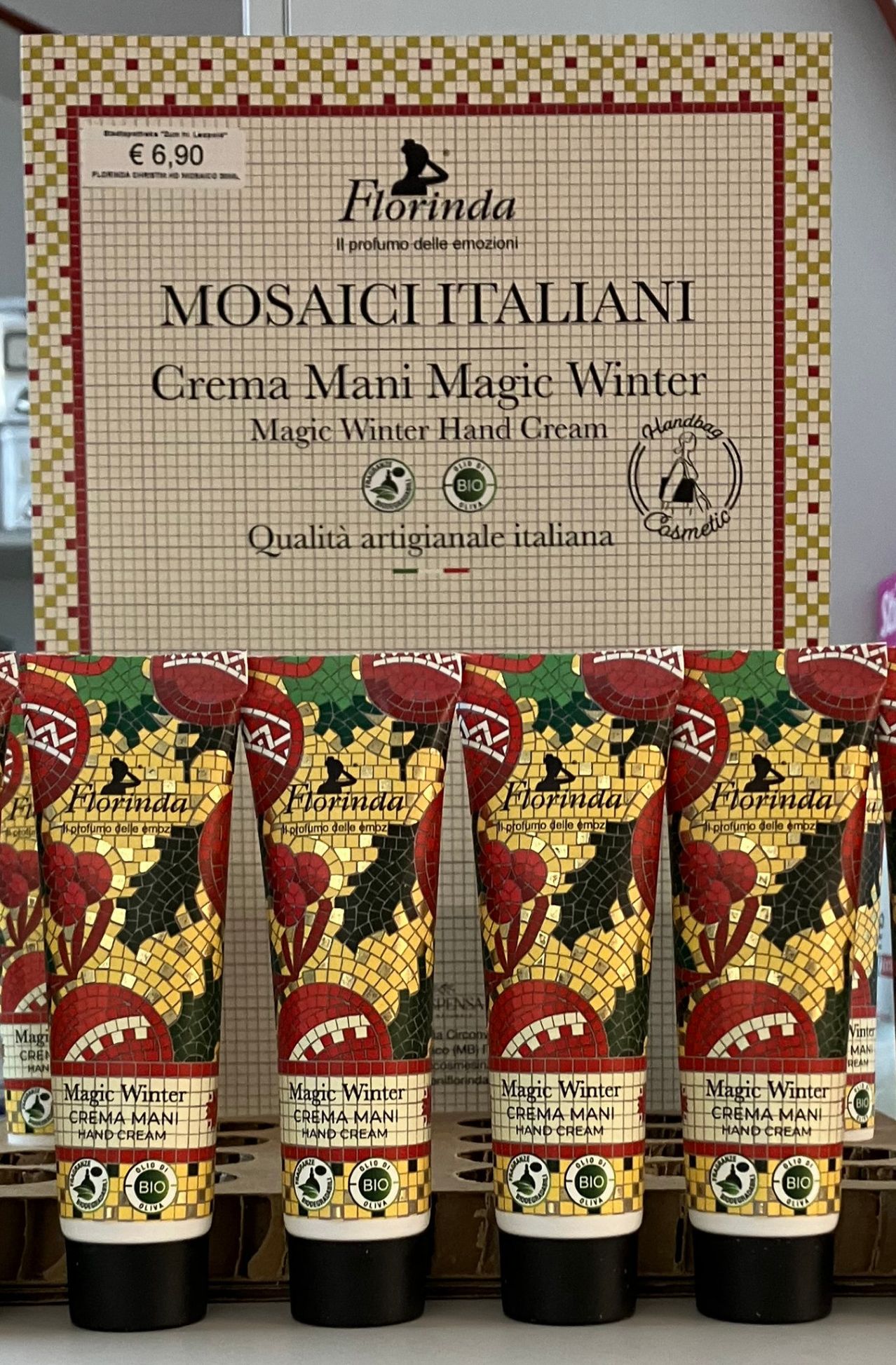 A row of six hand cream tubes is displayed in front of a mosaic-patterned sign. The brand name is Florinda, and the product name is Magic Winter Hand Cream. Each tube has a colorful mosaic design.