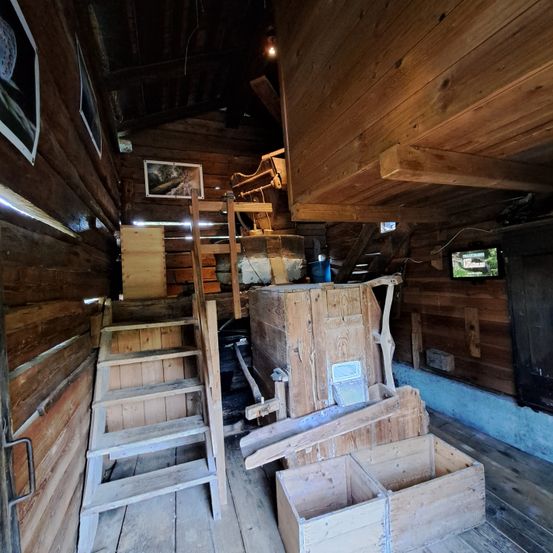 Das Innere eines Holzraumes mit Holztreppen, Regalen und Kisten. Es gibt einen Holzschrank und einen Bilderrahmen an der Wand.