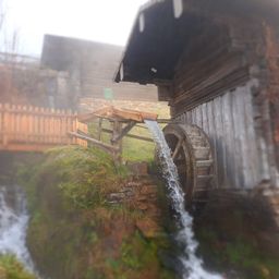 Eine alte Holzmühle mit einem Wasserrad, das von fließendem Wasser angetrieben wird, in einer rustikalen Außenumgebung gelegen.