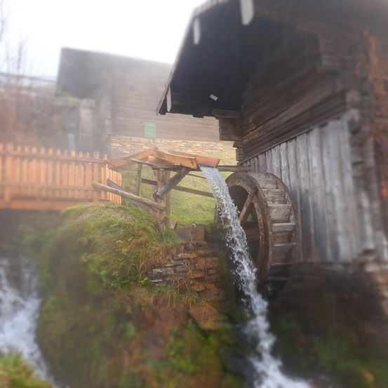 Eine alte Holzmühle mit einem Wasserrad, das von fließendem Wasser angetrieben wird, in einer rustikalen Außenumgebung gelegen.