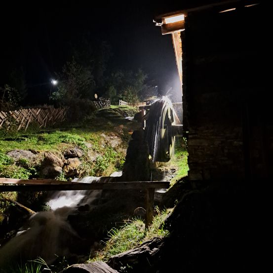 Ein Wasserrad, das in der Nacht von einem Licht beleuchtet wird, mit einem Strom, der davon fließt.