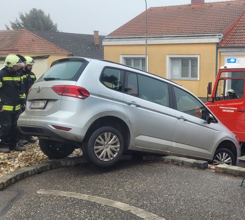 Ein silberner Volkswagen SUV steht schief auf dem Bordstein. Ein Feuerwehrfahrzeug ist daneben geparkt. Zwei Feuerwehrleute stehen in der Nähe.