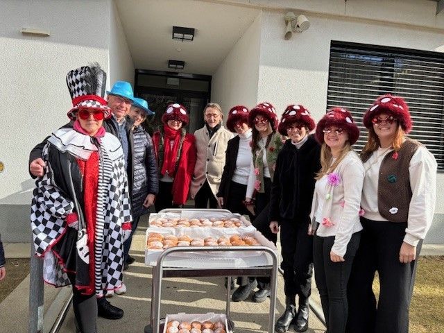 Eine Gruppe von Menschen in Kostümen steht vor einem Gebäude mit Tabletts voller Donuts auf einem Tisch.