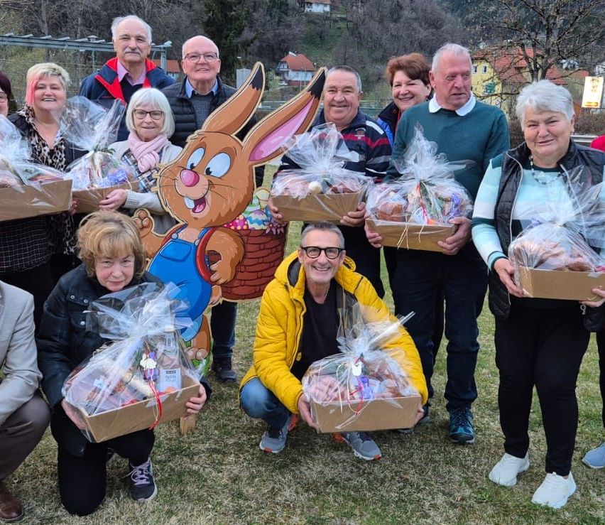 Eine Gruppe von Menschen, sowohl Männer als auch Frauen, posiert für ein Foto im Freien, während sie Osterkörbe halten. Sie stehen und knien auf dem Rasen.