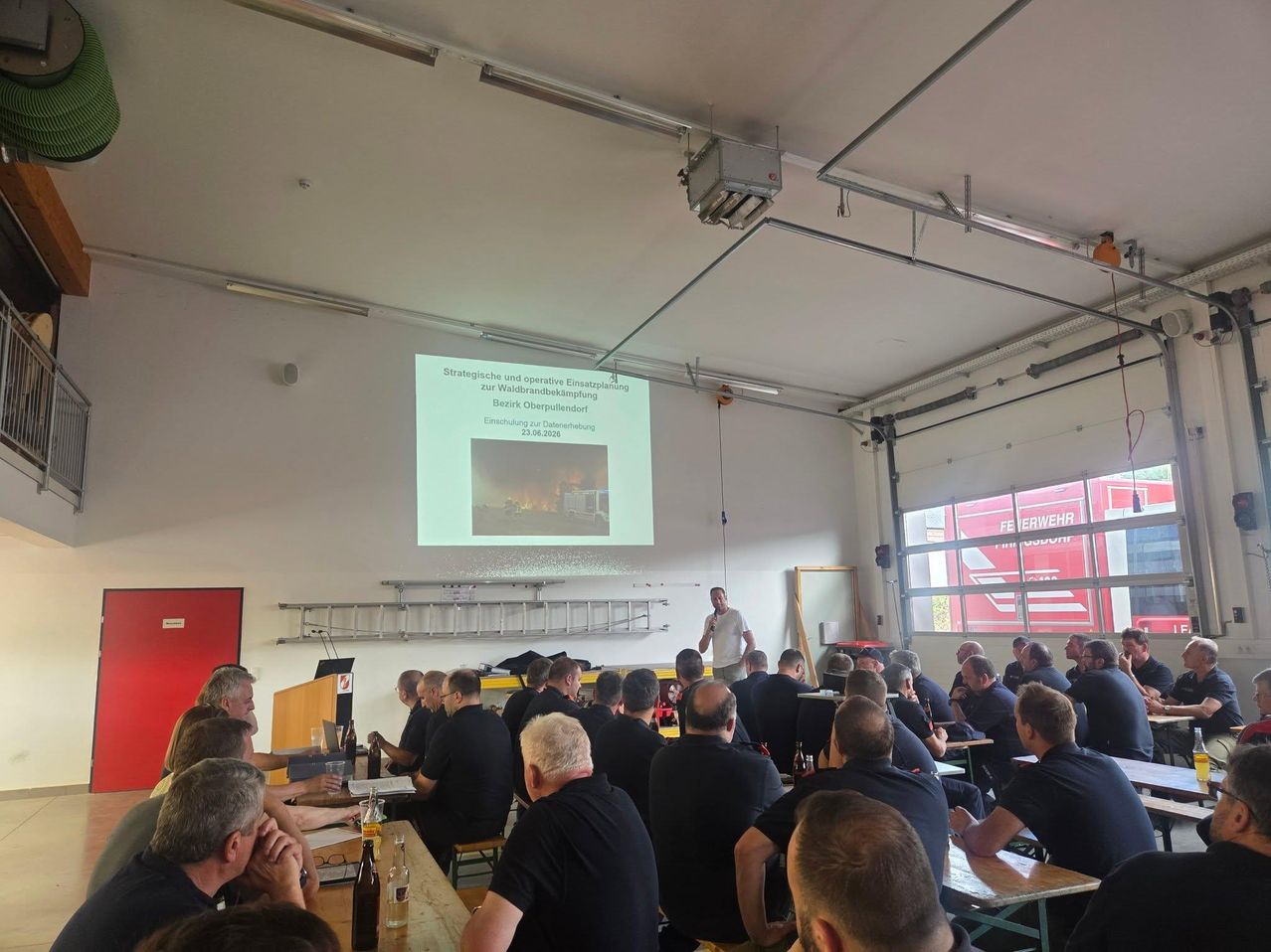 Ein Vortrag über strategische und operative Planung zur Waldbrandprävention wird von einem Mann in einem Klassenzimmer an einer Beamerwand gezeigt. Die Studenten hören aufmerksam zu.