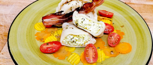 Ein grüner Teller mit drei gefüllten Teigtaschen, Speck, Tomaten und Käse auf einer Holzoberfläche.