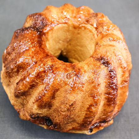 Ein glasierter Zimtschneckenkuchen liegt auf einem grauen Hintergrund. Die Oberseite ist mit karamellisiertem Glasur bedeckt und die Seiten sind leicht angebrannt.
