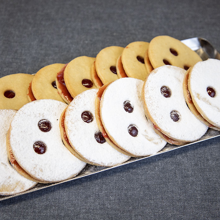 Ein Tablett mit Keksen, gefüllt mit Schokolade und roten Beeren, bestreut mit Puderzucker und in einem lächelnden Gesichtsmuster angeordnet.