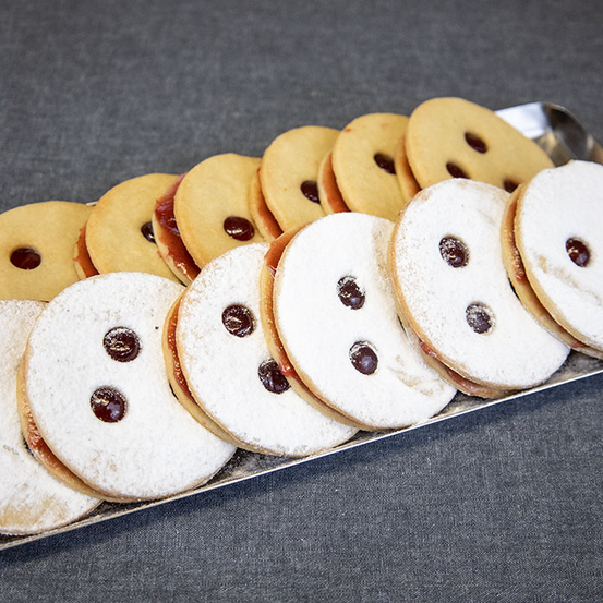 Ein Tablett mit Keksen, gefüllt mit Schokolade und roten Beeren, bestreut mit Puderzucker und in einem lächelnden Gesichtsmuster angeordnet.