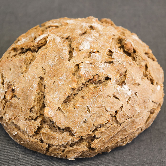 Ein rundes, braunes, rustikales Brot mit strukturierter Kruste, mit Mehl bestreut, ruht auf einer grauen Oberfläche.