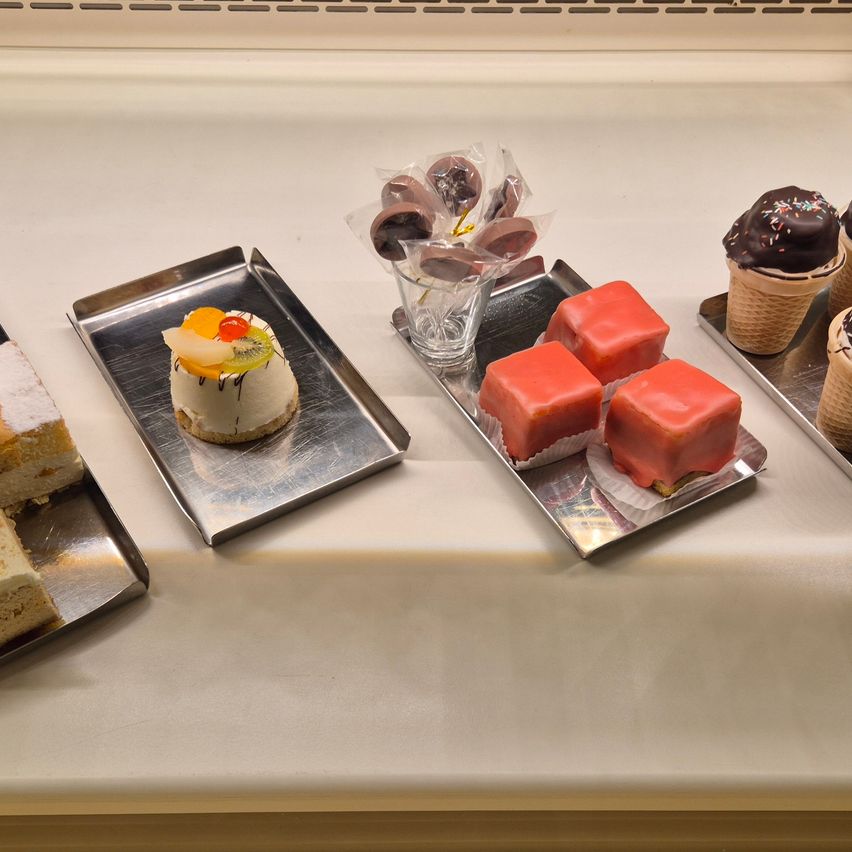 Eine Auswahl an Desserts auf Tabletts und Eistüten: ein kleiner Kuchen, ein Stück Kuchen, Schokoladenüberzogene Leckereien und ein Schokoladenüberzogener Eisbecher.