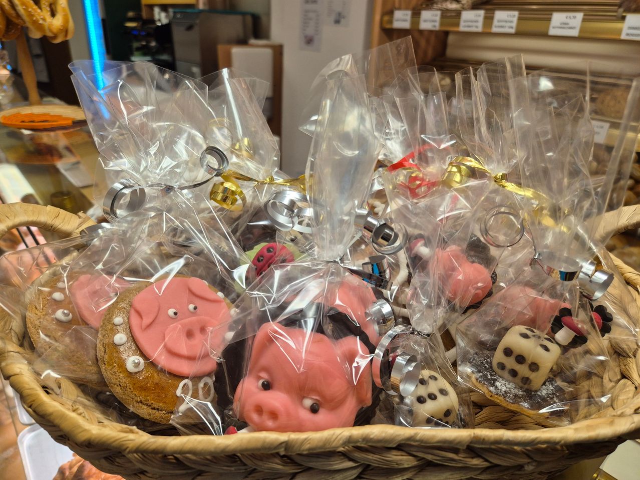Ein Korb voller in Plastik eingewickelter, schwein-thematischer Desserts mit Bändern und Würfeln auf einem Tisch.
