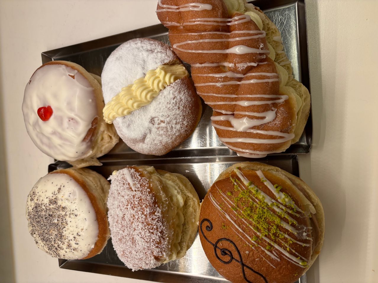 Ein Tablett mit verschiedenen Gebäckstücken, darunter ein glasierter Donut, ein pulverisierter Donut mit Zuckerguss, ein geflochtener Teig, ein mit Kokosnuss bestreuter Teig, ein Teig mit schwarzem Topping und ein Teig mit grünem Topping.