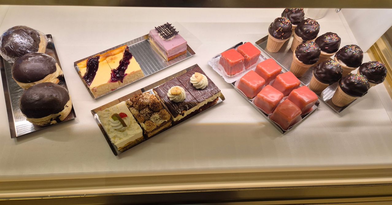 Eine Vitrine mit verschiedenen Desserts, darunter Käsekuchen, Biskuitkuchen und Eiswaffeln, ordentlich auf Tabletts angeordnet.