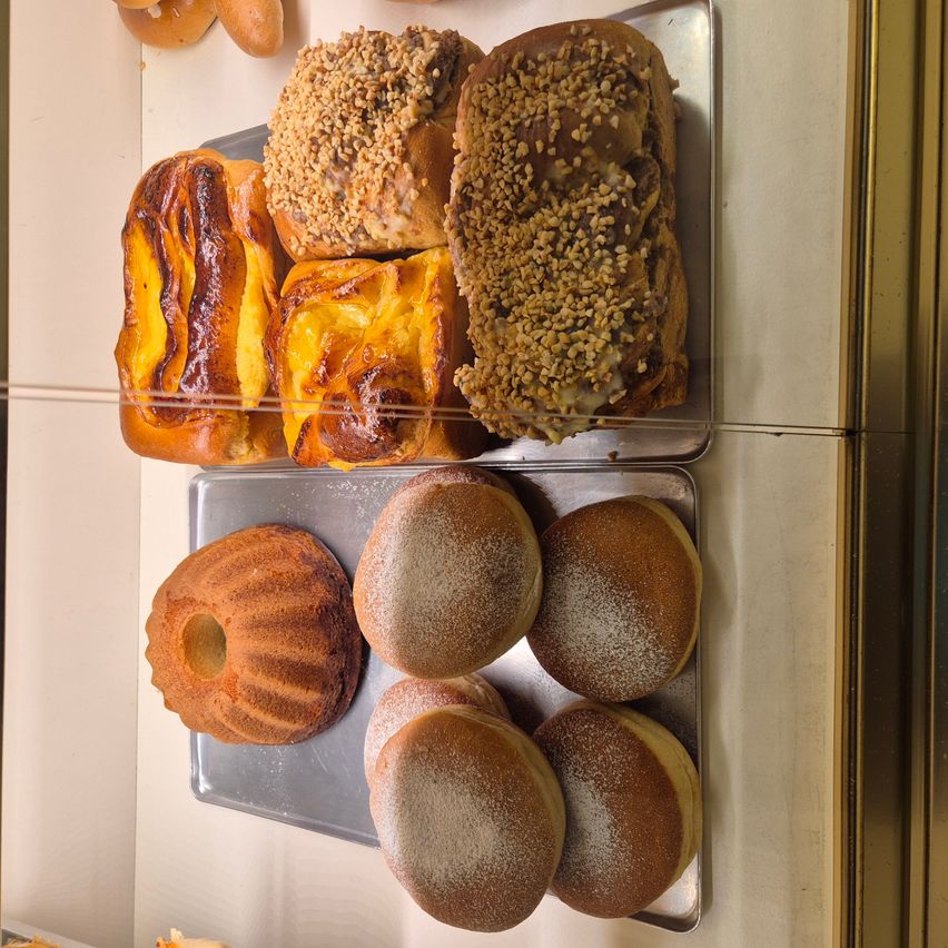 Ein Tablett mit verschiedenen Gebäckstücken, darunter ein Brot mit Nüssen, ein Brot mit Käse, ein Kuchen mit einer Öffnung und Donuts mit Puderzucker.