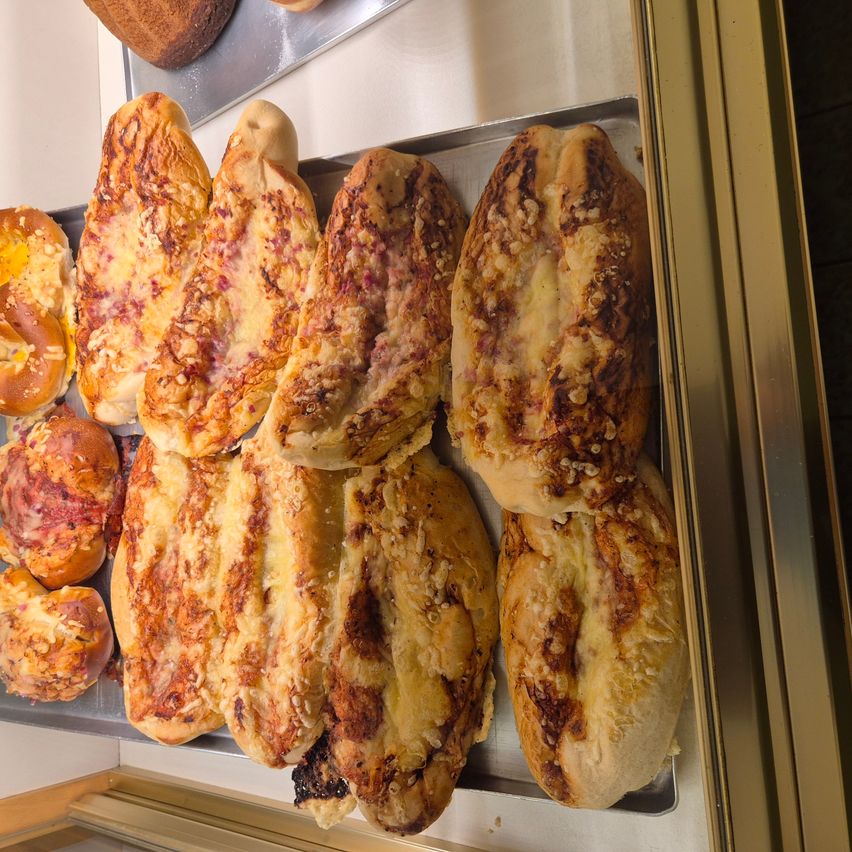 Ein Tablett mit verschiedenen Brotsorten, einschließlich solcher mit Käse, Fleisch und Nüssen, wird in einer Glasvitrine präsentiert.