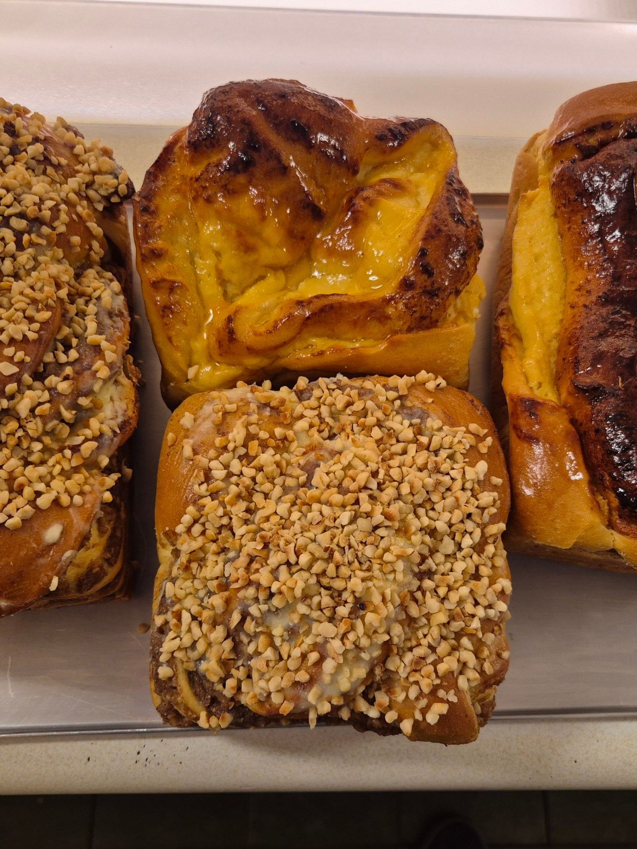 Ein Nahaufnahme von verschiedenen Gebäckstücken, darunter eines mit goldbrauner Kruste und einer Füllung, die süß zu sein scheint, und ein anderes, das mit Nüssen bestreut ist.