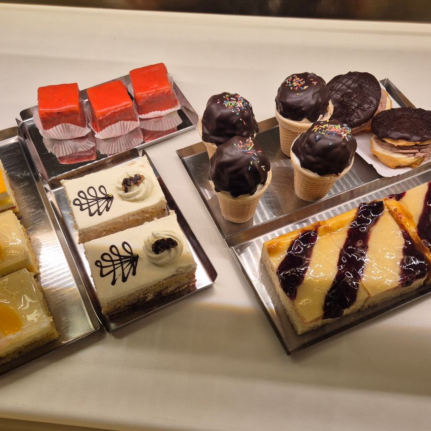 Eine Ausstellung verschiedener Desserts, darunter Schichtkuchen, mit Schokolade überzogene Eisbecher und ein mit Schokolade überzogenes Gebäck, auf Silberschalen angeordnet.