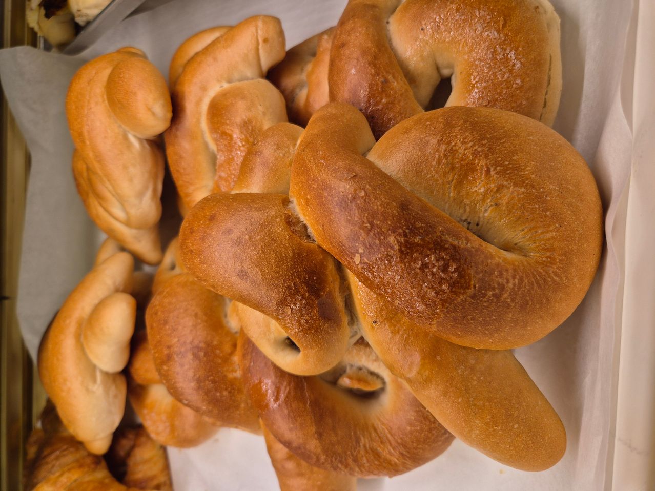 Ein Nahaufnahme von einem Stapel Brezeln, einige mit Löchern und andere ohne. Sie haben eine goldbraune Farbe, was darauf hindeutet, dass sie frisch gebacken sind.