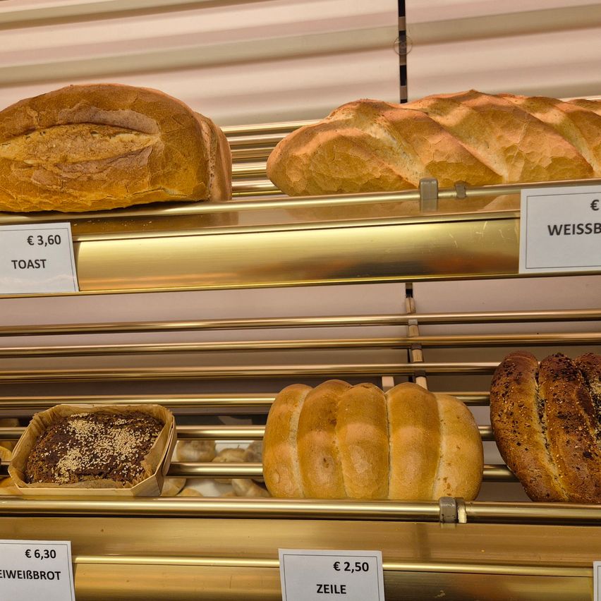 Eine Bäckerei-Auslage mit verschiedenen Brotsorten. In der oberen Reihe sind Toastbrot für 3,60 Euro und Weissbrot für 2,50 Euro. In der unteren Reihe sind Weissbrot für 6,30 Euro und ein Sesambrot.