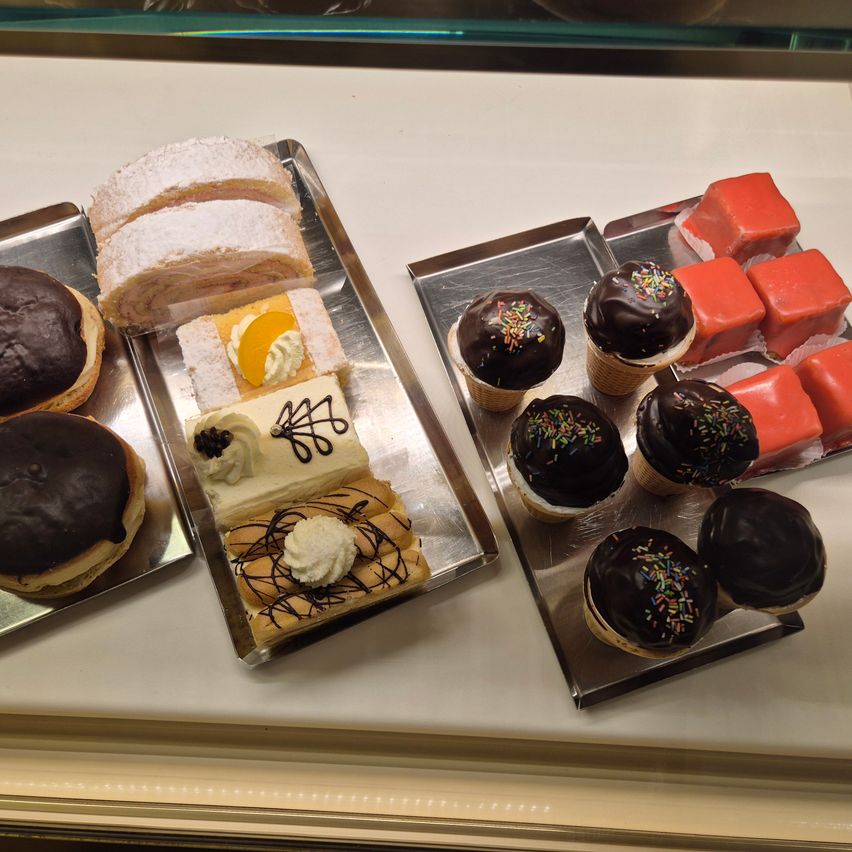 Eine Ausstellung verschiedener Desserts, darunter Schokoladen-Krapfen, ein Rollkuchen und mit Schokolade überzogene Cupcakes mit Streuseln auf einem silbernen Tablett.