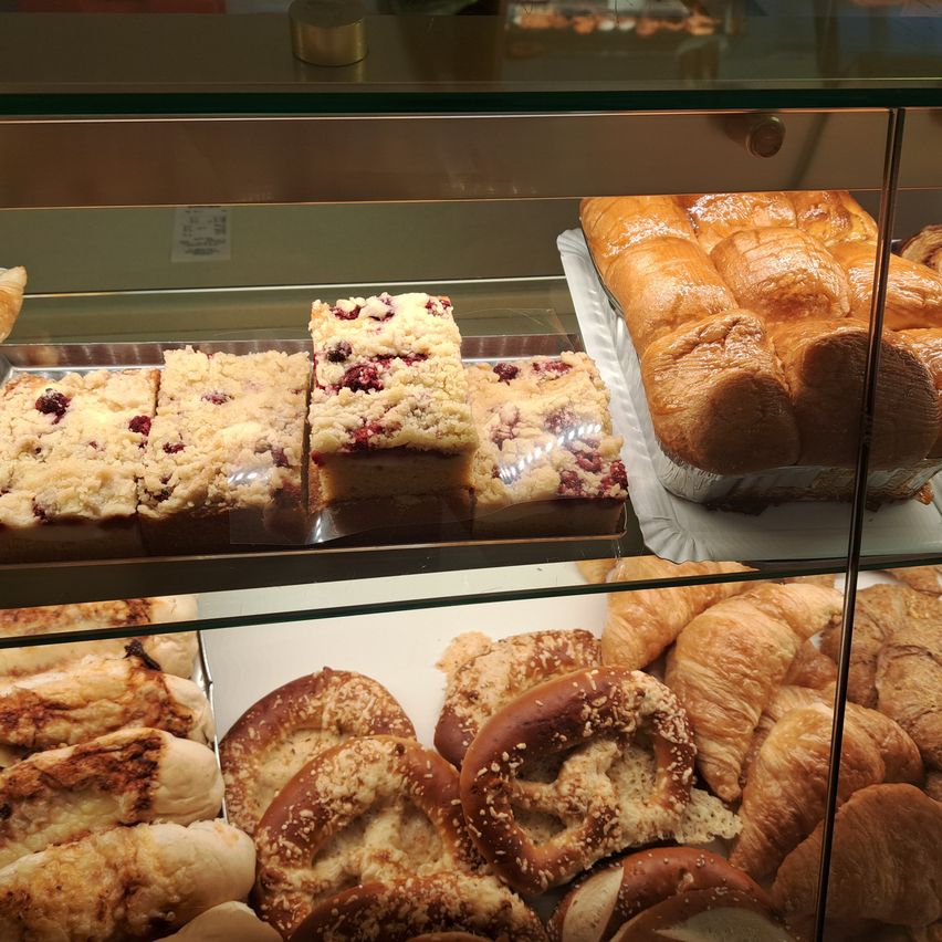 Ein Glasvitrine gefüllt mit verschiedenen Backwaren, darunter Brot, Croissants und Brezeln. Das Brot ist goldbraun und sieht frisch gebacken aus.