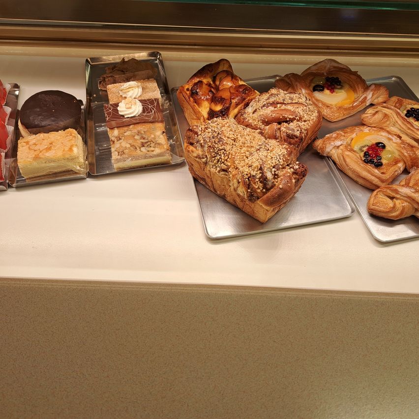 Eine Auswahl verschiedener Gebäcke, darunter Croissants, Obsttörtchen und mehrschichtige Kuchen, auf einem weißen Tresen.