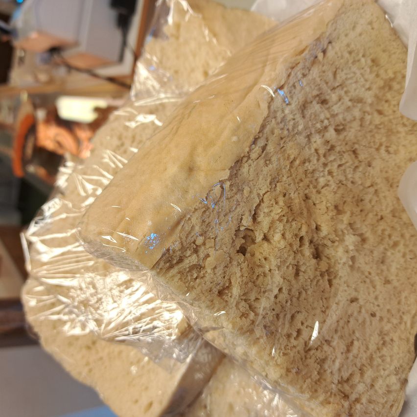 Mehrere Brotstücke sind in durchsichtige Plastikfolie eingewickelt. Die Textur erscheint rau und rustikal, was auf ein hausgemachtes oder handwerkliches Produkt hindeutet.
