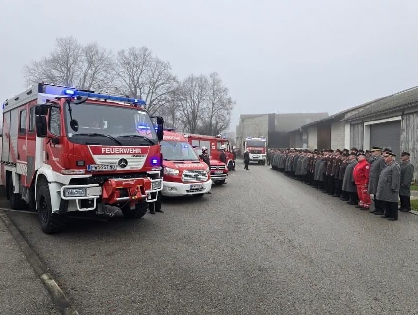Eine Reihe von Feuerwehrleuten und Feuerwehrfahrzeugen steht für eine Zeremonie an einem nebligen Tag bereit.
