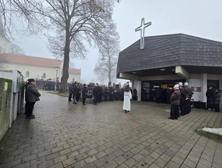 Eine Gruppe von Menschen, einschließlich uniformierter Polizisten, steht an einem nebligen Tag vor einer Kirche. Eine Frau in einem weißen Kleid steht davor.