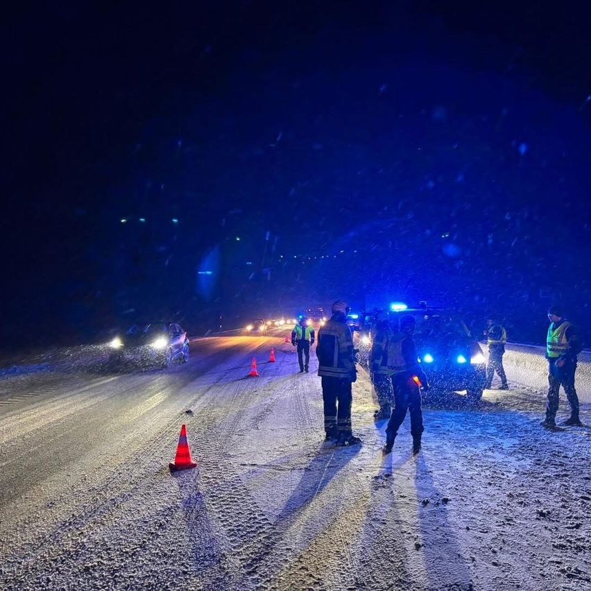 Polizeibeamte stehen bei Nacht im Schnee und leiten den Verkehr. Es sind Verkehrskegel und blinkende Polizeilichter zu sehen.