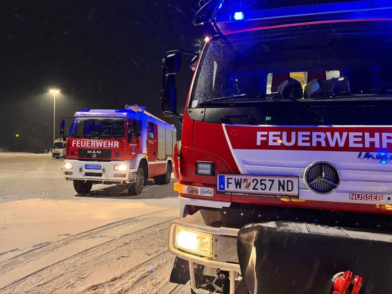 Zwei Feuerwehrfahrzeuge sind auf einer verschneiten Straße bei Nacht geparkt. Eines ist ein roter MAN-Lkw und das andere ist ein roter Mercedes-Benz mit dem Kennzeichen FW 257 ND.