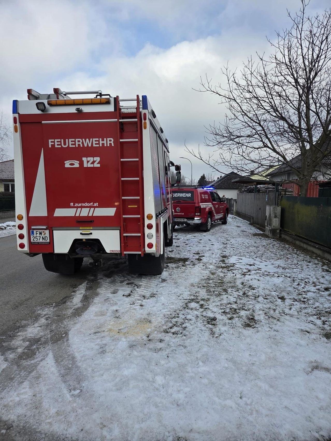 Ein roter Feuerwehrwagen mit der Nummer 122 ist am Rande einer verschneiten Straße geparkt. Ein roter Polizeiwagen ist in der Nähe geparkt.