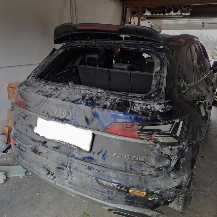 Ein beschädigter Audi Q5 TFSI SUV mit geöffnetem Heck, freiliegendem Kofferraum und sichtbaren Schäden, in einer Garage geparkt.