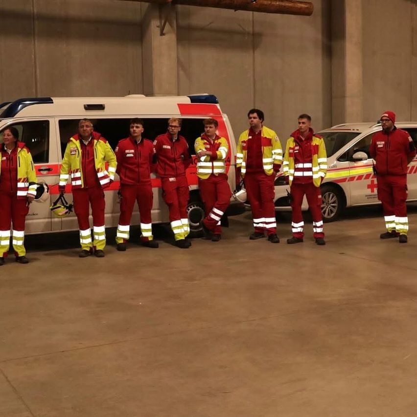 A group of first responders in red and yellow uniforms stand in front of two ambulances. They are inside a garage.