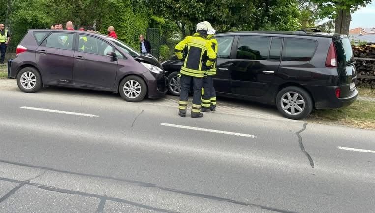 A car accident occurred on a street, with two cars parked and emergency workers present.