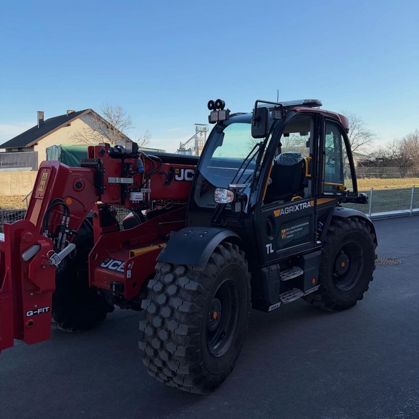 A red JCB AgriXtra telehandler is parked on a road with a house and trees in the background.