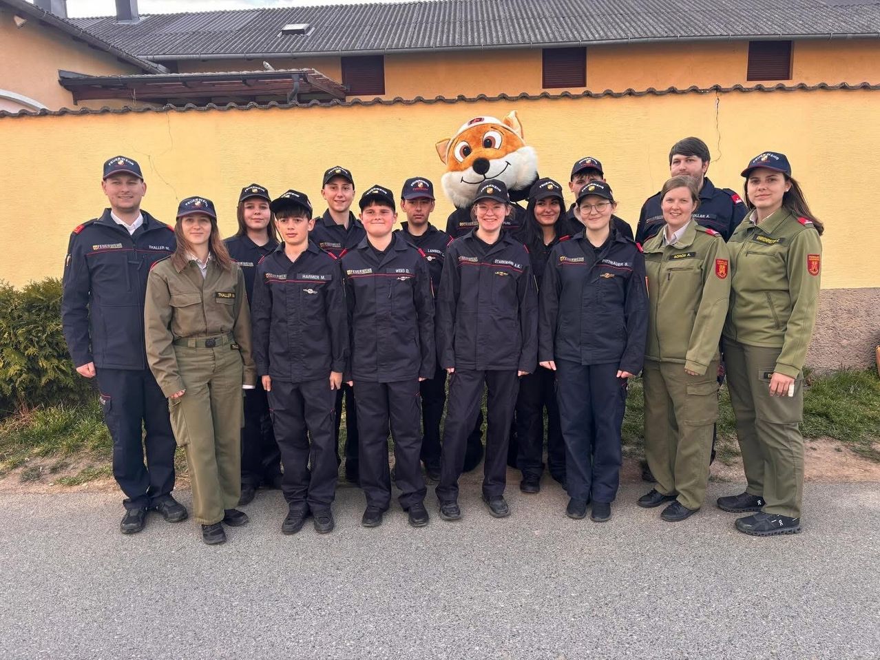 Eine Gruppe von Menschen in Uniform steht vor einem Gebäude mit einem Maskottchen-Fuchs und posiert für ein Gruppenfoto.