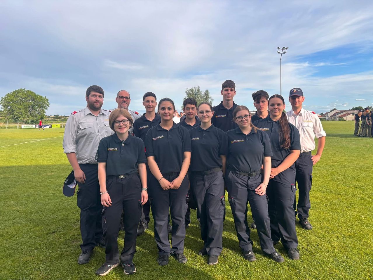 A group of people in matching uniforms stands on a field with a cloudy sky in the background.