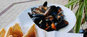 Ein weißer Teller mit Muscheln in einer Brühe, serviert mit geröstetes Brot auf der Seite, auf einem Ziegelboden platziert.