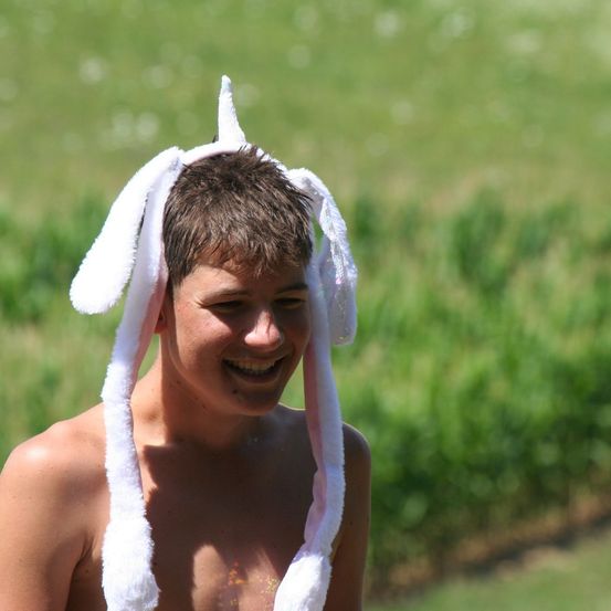 Ein junger Junge ist draußen und lächelt. Er trägt eine Einhornmütze. Der Hintergrund ist ein Grasfeld.