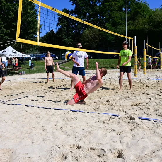 Eine Gruppe von Menschen spielt Volleyball auf einem sandigen Strand. Ein Spieler taucht, um den Ball zu schlagen.