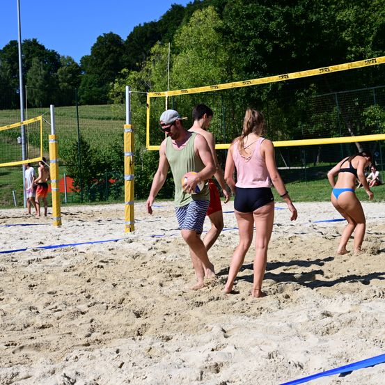 Eine Gruppe von Menschen spielt Volleyball auf einem sandigen Strand mit einem gelben Netz zwischen ihnen.